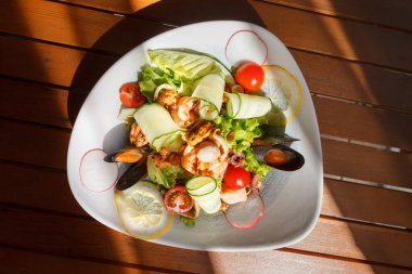 Sebzeli deniz ürünleri salatası. Alçak akşam güneşinin ışınları altında, tahta bir masanın üzerinde beyaz bir tabakta. Düz yatış, üst görünüm