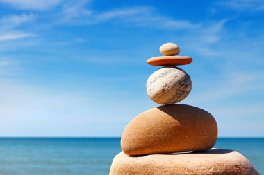 Taşlar mavi gökyüzü ve denizin arka planında dengelenir. Denge ve uyum kavramı. Rock zen