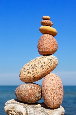 Denizin arka planındaki kumsalda renkli çakıl taşlarından oluşan bir taş zen piramidi. Yaşam dengesi, uyum ve meditasyon kavramı