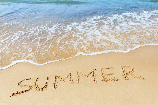 The word "Summer" written on the sand at the edge of the sea. The concept of summer vacation and good mood