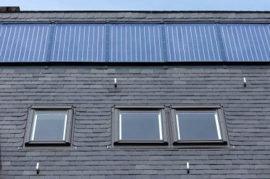 Siyah döşeme kiremitleri, çatı pencereleri ve sabit güneş panelleri