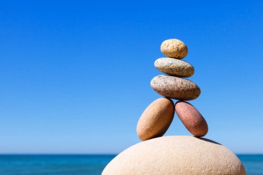 Denizin arka planındaki kumsalda renkli çakıl taşlarından oluşan bir taş zen piramidi. Yaşam dengesi, uyum ve meditasyon kavramı
