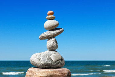 Taşlar mavi gökyüzü ve denizin arka planında dengelenir. Denge ve uyum kavramı. Rock zen