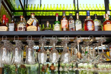 Singapur, Singapur-28 Kasım 2019: şarap bardakları bar tezgahının üzerinde alkollü içeceklerle dolu şişelerin arkasında asılı duruyor. Yumuşak odaklı, seçici odaklı