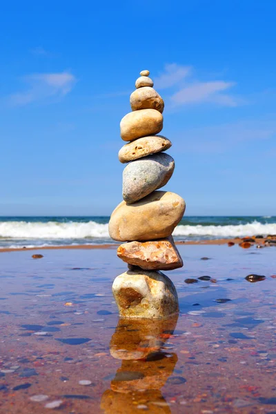 Rock zen pyramid of colorful pebbles standing in the water on the background of the sea. Concept of balance, harmony and meditation