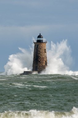 Huge waves break around the stone tower of Whalback lighthouse in Maine during rare high tide. clipart