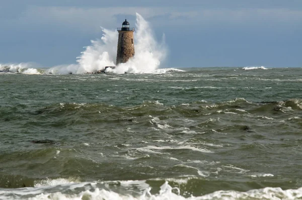 Giant waves surround stone lighthouse tower of Whalback light in Maine during a unique high tide.