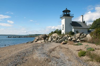 Bristol Ferry lighthouse is surrounded with large boulders to protect the keepers when the tides would rise in Narragansett Bay in Rhode Island. Beach area is covered with open shells at low tide. clipart