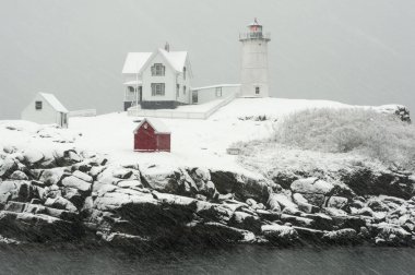 Nubble lighthouse, also known as Cape Neddick light, flashes its red light during a blizzard snowstorm in Maine, in New England. clipart