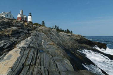 Dalgalar kayalık sahil şeridi boyunca kırılır. Pemaquid Point deniz feneri, Maine sahiline gelen ziyaretçilerin en sevdiği metaforik kaya oluşumlarının üzerinde yer almaktadır..