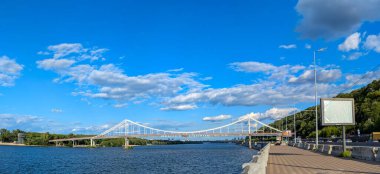 Yaya geçidi süspansiyon yapıları. Dinyeper Nehri 'nin üzerinde harika bir mavi gökyüzü manzarası ve ön planda yumuşak dalgalar olan bir köprü. Harika zikzak yansıması açıklıkları ve suda destek. Site için muhteşem duvar kağıdı ve afiş.