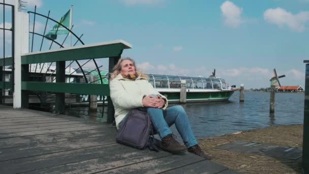 Old woman in white jacket is relaxing at ferry point with Dutch windmills in background