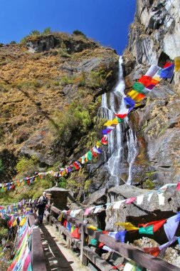 Holy waterfall with colorful Buddhist prayer flags at Taktshang Goemba or Tiger's nest monastery in Paro, Bhutan clipart