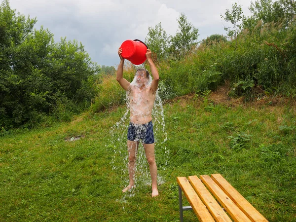 Man Stands Barefoot Grass Pours Cold Water Red Bucket — Stock Photo, Image