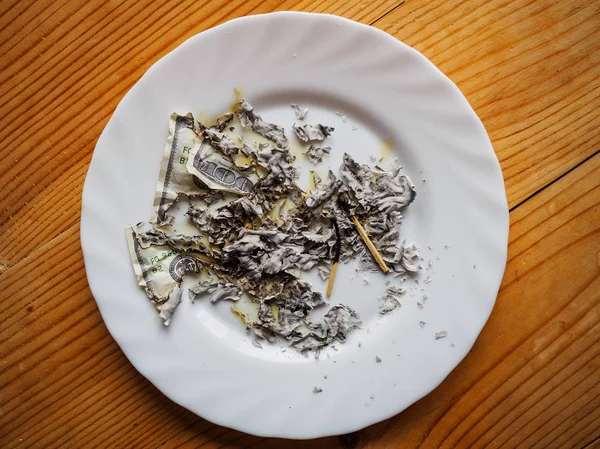 ashes from the burned dollars and their underburned remains on a white plate