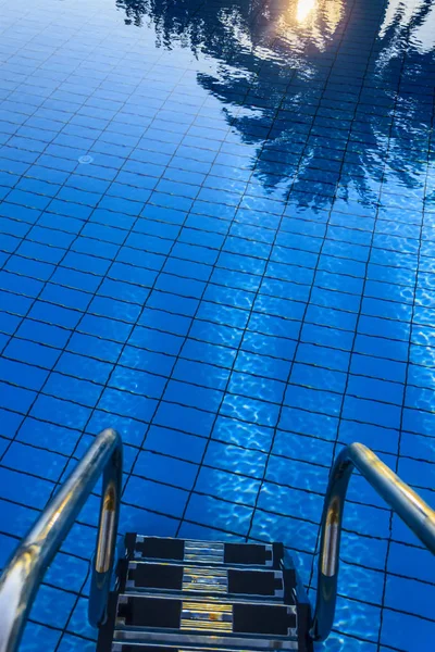 带楼梯的游泳池 蓝天上的太阳 泳池表面棕榈树之间的日落倒影 — 图库照片