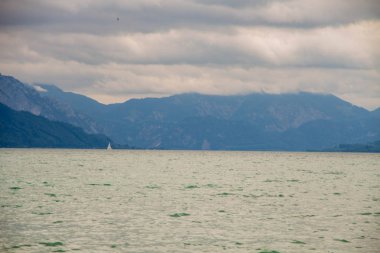 Attersee 'nin göl kenarında sakin bulutlu bir gün ve yazın sonlarında arka planda dağlar. Attersee Gölü Avusturya Salzkammergut 'unda