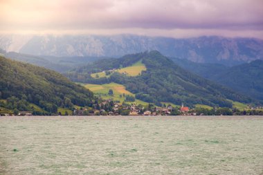Attersee 'nin göl kenarında sakin bulutlu bir gün ve yazın sonlarında arka planda dağlar. Attersee Gölü Avusturya Salzkammergut 'unda