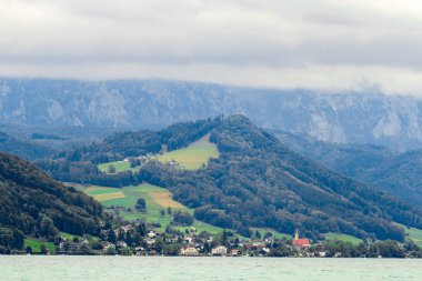Attersee 'nin göl kenarında sakin bulutlu bir gün ve yazın sonlarında arka planda dağlar. Attersee Gölü Avusturya Salzkammergut 'unda
