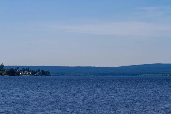 A Lipno Dam-Horni Plana, Cseh Köztársaság, egy világos nyári napon. A tó nyugodt, tiszta kék vízzel. Nincsenek felhők az égen. Sok fa a háttérben. — Stock Fotó