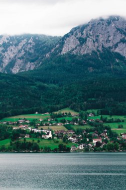 Attersee 'nin göl kenarında sakin bulutlu bir gün ve yazın sonlarında arka planda dağlar. Attersee Gölü Avusturya Salzkammergut 'unda