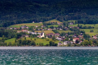 Attersee 'nin göl kenarında sakin bulutlu bir gün ve yazın sonlarında arka planda dağlar. Attersee Gölü Avusturya Salzkammergut 'unda
