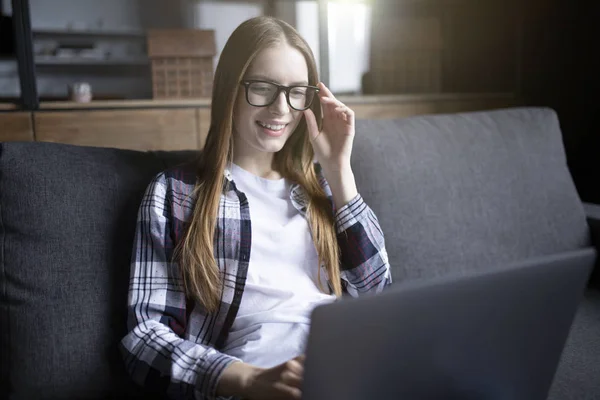 Porträtt av en söt flicka i glasögon med en laptop i soffan — Stockfoto