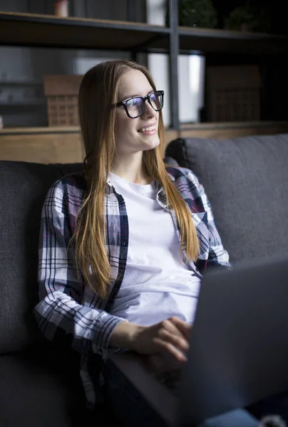 Porträtt av en söt flicka i glasögon med en laptop i soffan — Stockfoto