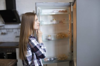 Güzel kız buzdolabı açar ve ne yemek düşünüyor