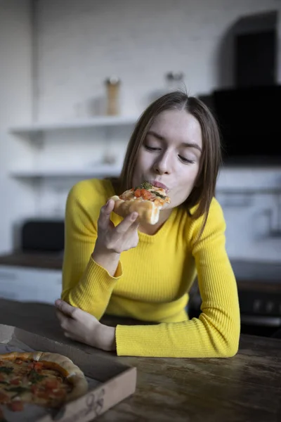 Grappig brunette meisje in gele trui eten pizza in de keuken — Stockfoto