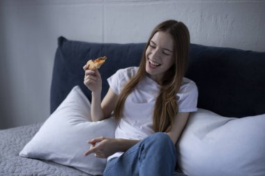 Mutlu genç kadın evde sıcak pizza dilim yemek ve izliyor