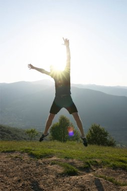 Genç adam güzel dağların arka planında güneşli bir ışıkla zıplıyor.