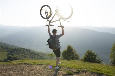 Genç adam bir bisikletle dağın arka planında duruyor.