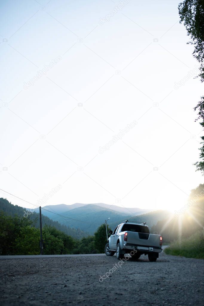 Pickup truck in the background of mountains with a sun glare. Beautiful car is driving along the road in the forest