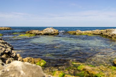 Gün batımı sahne arka planda kayalar ile mavi gökyüzü ve deniz. Kayalar ve taşlar arasında gün batımı çakıl deniz plajı.