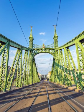 Macaristan 'ın Budapeşte kentindeki Özgürlük Köprüsü, açık mavi gökyüzünün altında, ikonik yeşil yapısını ve tramvay hatlarını gözler önüne seriyor..
