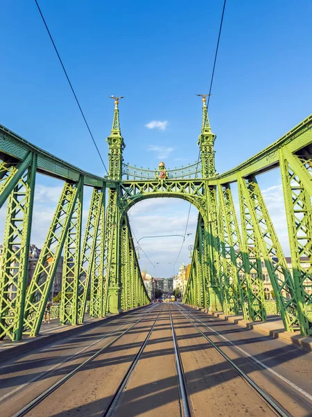 Macaristan 'ın Budapeşte kentindeki Özgürlük Köprüsü, açık mavi gökyüzünün altında, ikonik yeşil yapısını ve tramvay hatlarını gözler önüne seriyor..