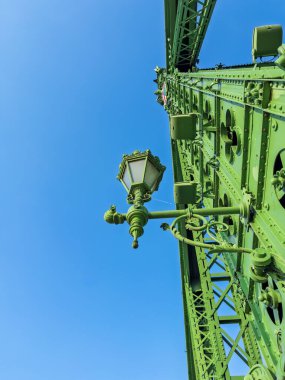 Liberty Köprüsü 'ne karmaşık metal işçiliği ve parlak mavi arkaplanı olan klasik dekoratif fener. Süslü yeşil çelik köprüye geleneksel sokak aydınlatma armatürü. . 