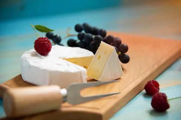 Sýr camembert s malinami a hrozny na modrém pozadí — Stock fotografie