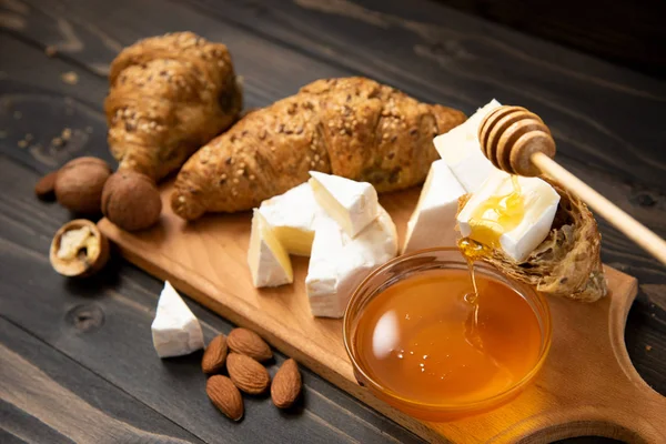 dilim peynir brie veya camembert kruvasan, bal ve koyu ahşap arka plan üzerinde kesim için gemide fındık ile