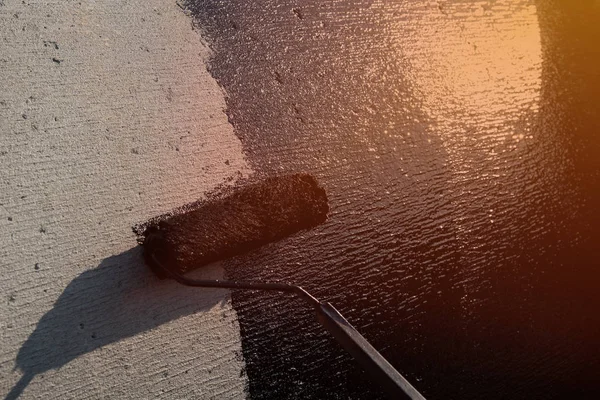 Roofer worker painting black coal tar or bitumen