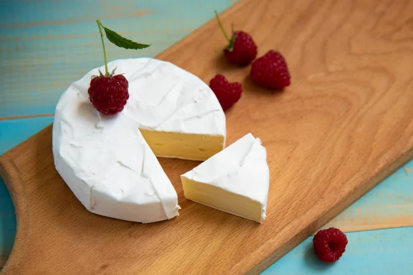 Camembert de queijo com framboesas em uma mesa azul — Fotografia de Stock