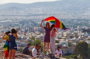 Atina, Yunanistan - 9 Haziran 2018: diğer turistlerin bakmak gibi bir kayanın üzerinde onların arkadaşları tarafından arasında Acropolis fotoğraflandı edilmektedir Atina gurur 2018 gününde bayrak tutan kızlar