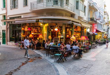 Athens, Greece - June 9, 2018: Atmospheric scene of people sitting at an Athens cafeteria late on a summer afternoon clipart