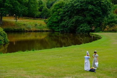 Stockport, Büyük Britanya - 24 Temmuz 2018: iki kız Lyme Hall, tarihi İngilizce görkemli ev Cheshire, bir cep telefonu kullanarak parkta Lyme içinde Edwardian kostümleri!