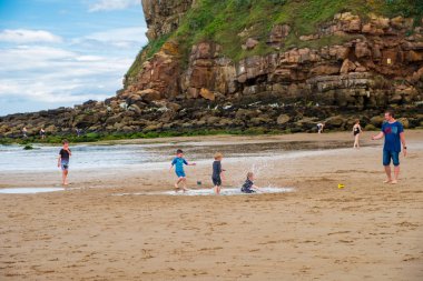 Tynemouth, England - August 2, 2018: Boys playing at King Edward's Bay beach on a hot partly cloudy summer day. clipart