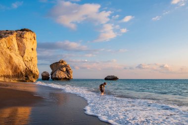 Paphos, Kıbrıs - 24 Kasım 2018: A yalınayak çocuk Petra tou Romiou kayalar, Paphos, Kıbrıs için plajda oynamaktadır. Plaj Yunan mitolojisinde Afrodit'ın Doğum yeri olarak kabul edilir.