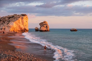 Paphos, Kıbrıs - 24 Kasım 2018: Bir çocuk sahilde Petra tou Romiou kayalar, Paphos, Kıbrıs için oynamaktadır. Plaj Yunan mitolojisinde Afrodit'ın Doğum yeri olarak kabul edilir.