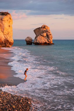 Paphos, Kıbrıs - 24 Kasım 2018: Bir çocuk sahilde Petra tou Romiou kayalar, Paphos, Kıbrıs için oynamaktadır. Plaj Yunan mitolojisinde Afrodit'ın Doğum yeri olarak kabul edilir.