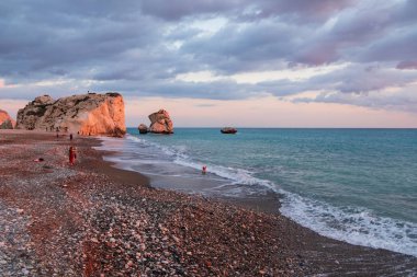 Paphos, Kıbrıs - 24 Kasım 2018: İnsanlar kendilerini Petra tou Romiou içinde banyo öğleden sonra ışık, Paphos, Kıbrıs'ta kayalar karşı sahilde tadını çıkarın. Plaj Yunan mitolojisinde Afrodit'ın Doğum yeri olarak kabul edilir.